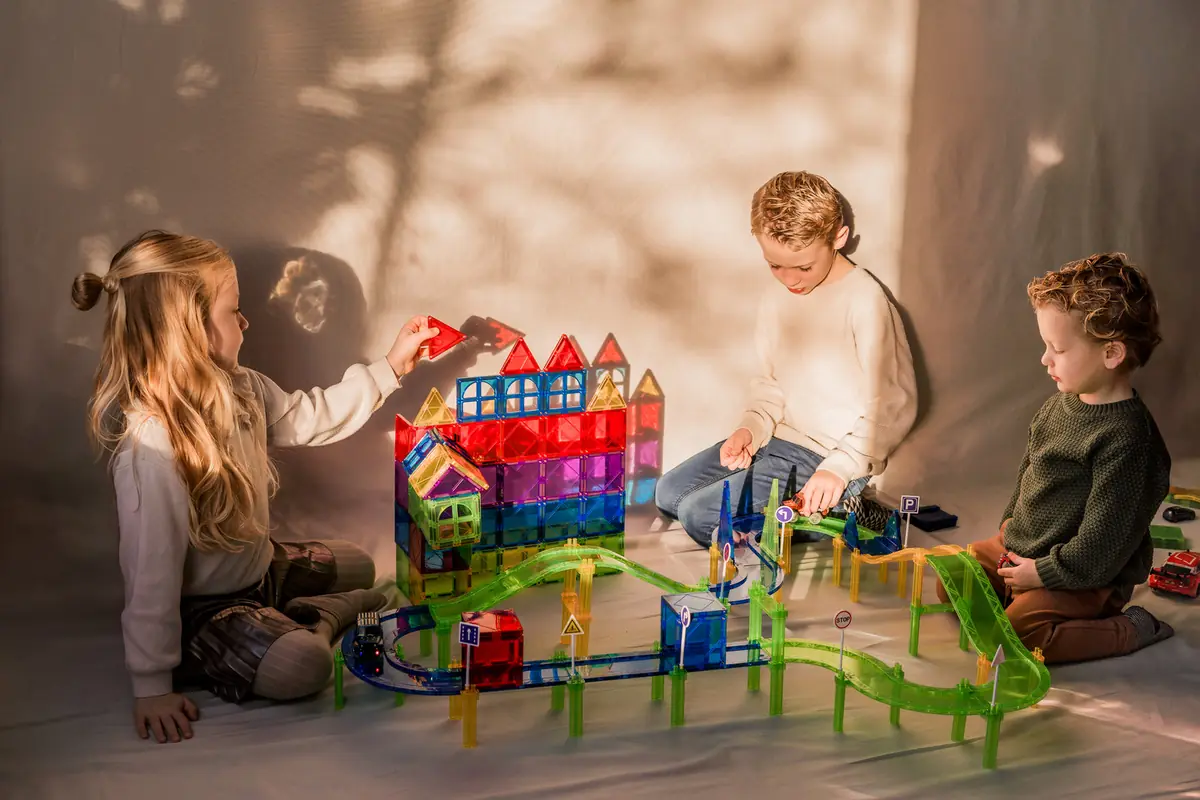 Drie kinderen spelen samen met magnetische tegels en een racebaan