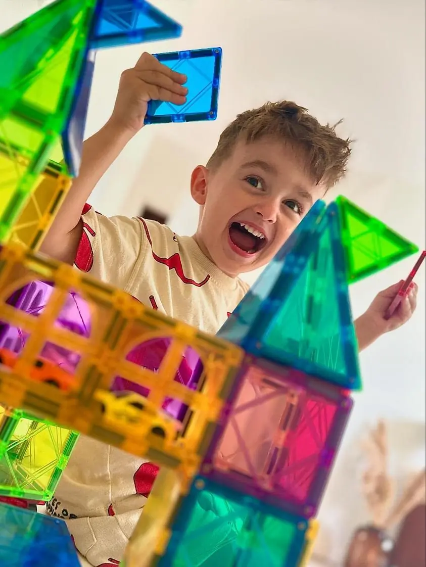 Jongen lacht terwijl hij met magnetische tegels bouwt