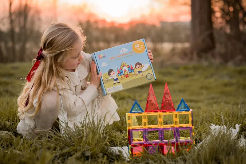 Meisje zit in het gras naast een bouwwerk en een doos magnetische tegels