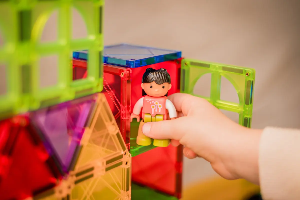 Kinderhand zet een poppetje in een huis van magnetische tegels